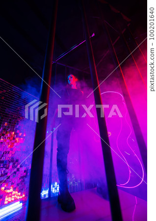 Caucasian woman in neon studio behind steel bars.  100201640