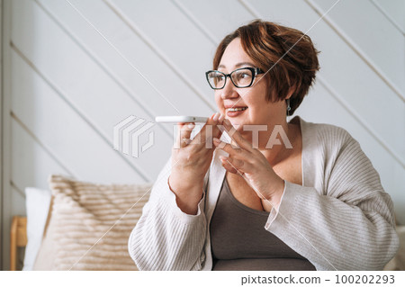 Smiling middle aged plus size woman using mobile phone on bed at home Smiling middle aged plus size woman using mobile phone on bed at home 100202293