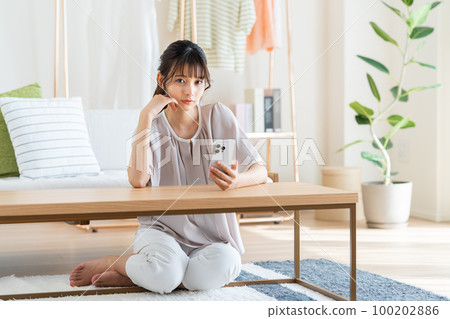 Young woman looking at her smartphone in the living room Young woman looking at her smartphone in the living room 100202886