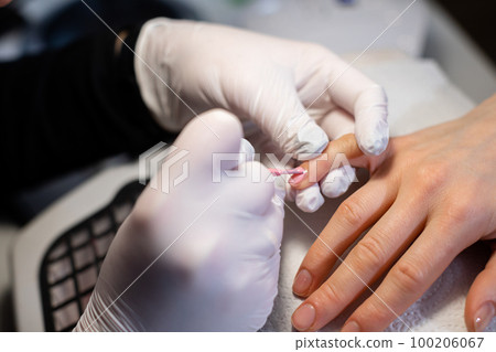 The beautician paints the nail of the client's little finger. 100206067