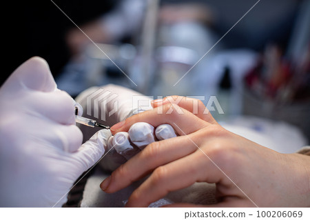 A beautician paints the nail of a client's ring finger 100206069