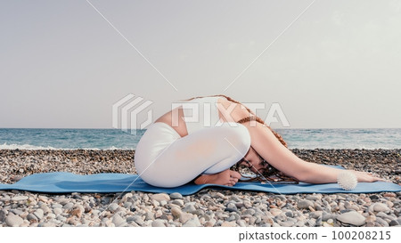 Woman sea yoga. Well looking middle aged woman with braids dreadlocks in white leggings and tops doing stretching pilates on yoga mat near sea. Female fitness yoga routine concept. Healthy lifestyle. Woman sea yoga. Well looking middle aged woman with braids dreadlocks in white leggings and tops doing stretching pilates on yoga mat near sea. Female fitness yoga routine concept. Healthy lifestyle. 100208215
