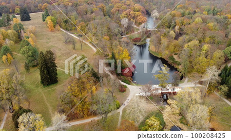 Beautiful landscape view of autumn park with lakes with swans, trees with yellow red green leaves, meadow, architecture, waterfall and people walking along dirt paths on autumn day. Natural background Beautiful landscape view of autumn park with lakes with swans, trees with yellow red green leaves, meadow, architecture, waterfall and people walking along dirt paths on autumn day. Natural background 100208425