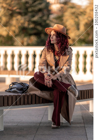 Outdoor fashion portrait of young elegant fashionable brunette woman, model in stylish hat, choker and light raincoat posing at sunset in European city. Outdoor fashion portrait of young elegant fashionable brunette woman, model in stylish hat, choker and light raincoat posing at sunset in European city. 100208432