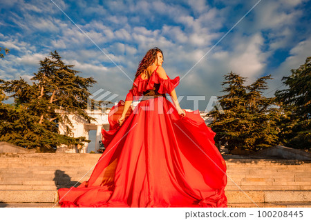 Sunrise red dress. A woman in a long red dress against the backdrop of sunrise, bright golden light of the sun's rays. The concept of femininity, harmony. 100208445