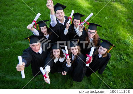 Graduates in robes show off their diplomas outdoors. View from above. Age student. 100211368
