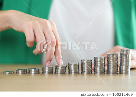 Fingers of business woman walk through stacks of coins on wooden desk. 100211469