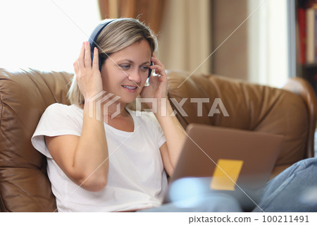 Woman with headphones and computer talking online while sitting on couch. 100211491