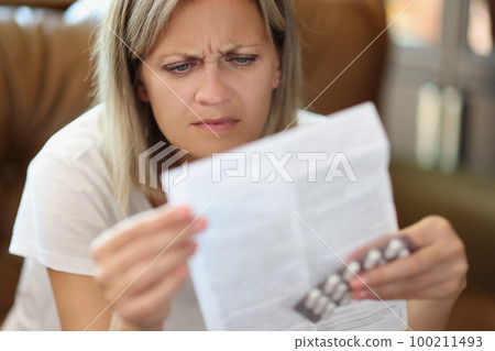 Woman with serious face reads doctor's prescription while sitting on sofa. Woman with serious face reads doctor's prescription while sitting on sofa. 100211493