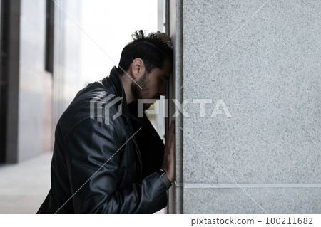 young man feels angry while standing with his head to the wall of the building 100211682