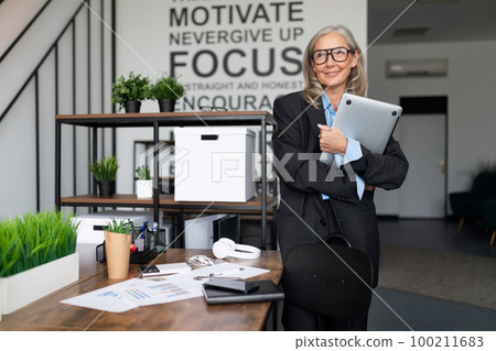 portrait of successful mature adult female boss standing in company portrait of successful mature adult female boss standing in company 100211683