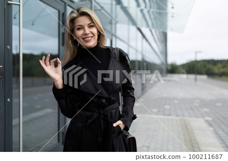 young woman investor shows a sign of trust with her hands on the background of a business center 100211687