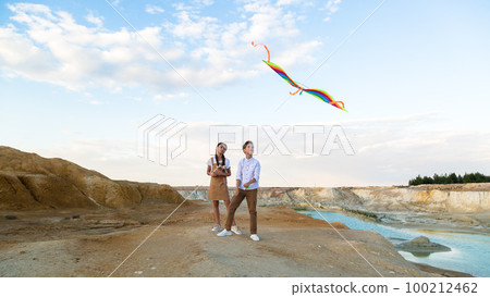 A boy and a girl launch a bright kite standing on the edge of a mountain near a pond 100212462