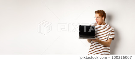 Young redhead man look impressed, showing laptop empty screen with logo banner. Guy in glasses checking out online advertisement on computer, white background Young redhead man look impressed, showing laptop empty screen with logo banner. Guy in glasses checking out online advertisement on computer, white background 100216007