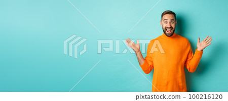 Excited man react to promo offer, spread hands sideways and rejoicing, standing against turquoise background in orange sweater Excited man react to promo offer, spread hands sideways and rejoicing, standing against turquoise background in orange sweater 100216120