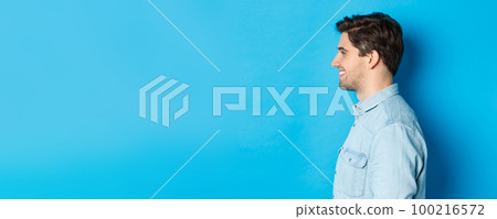 Profile of handsome young man looking left, smiling happy, standing over blue background 100216572