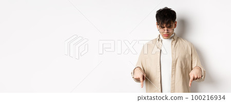 Confused frowning guy in glasses looking, pointing fingers down at something strange, standing puzzled on white background Confused frowning guy in glasses looking, pointing fingers down at something strange, standing puzzled on white background 100216934