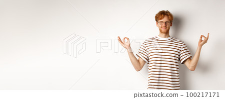 Calm and relaxed young man with red messy hair, spread hands sideways in mudra gesture and smiling, practice yoga or meditating, white background Calm and relaxed young man with red messy hair, spread hands sideways in mudra gesture and smiling, practice yoga or meditating, white background 100217171