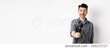 Handsome smiling man stretch out hand with microphone, giving you mic, standing on white background Handsome smiling man stretch out hand with microphone, giving you mic, standing on white background 100217217