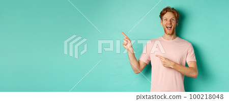 Cheerful caucasian man in t-shirt looking happy, pointing fingers left and showing promo offer, standing over turquoise background 100218048