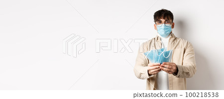 Health, covid and quarantine concept. Image of young guy handing out medical masks for preventive measures, helping during pandemic, standing on white background Health, covid and quarantine concept. Image of young guy handing out medical masks for preventive measures, helping during pandemic, standing on white background 100218538