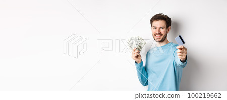 Smiling caucasian man holding money and giving you plastic credit card, standing on white background Smiling caucasian man holding money and giving you plastic credit card, standing on white background 100219662