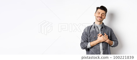 Romantic happy man holding hands on heart and smiling with closed eyes, dreaming of something, feeling nostalgic from sweet memories, standing on white background Romantic happy man holding hands on heart and smiling with closed eyes, dreaming of something, feeling nostalgic from sweet memories, standing on white background 100221839