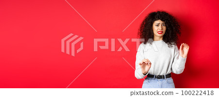 Disgusted and reluctant woman say no, raising hands to block or refuse, asking to stop, looking uncomfortable, standing on red background 100222418