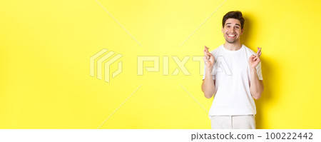 Hopeful smiling man holding fingers crossed, making wish or praying, standing over yellow background Hopeful smiling man holding fingers crossed, making wish or praying, standing over yellow background 100222442