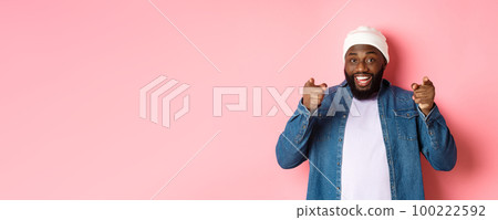 Happy african-american hipster guy pointing at camera, need you, smiling and inviting to company, standing over pink background 100222592