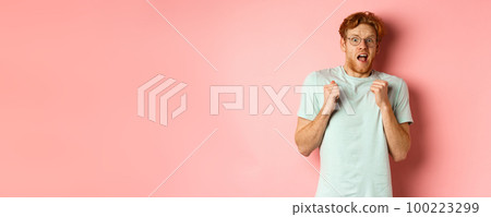 Portrait of scared redhead guy in glasses staring startled at camera, press hands to body and scream of fear, standing over pink background Portrait of scared redhead guy in glasses staring startled at camera, press hands to body and scream of fear, standing over pink background 100223299