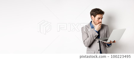 Shocked office worker in suit looking worried at laptop screen, having trouble at work, standing on white background 100223495