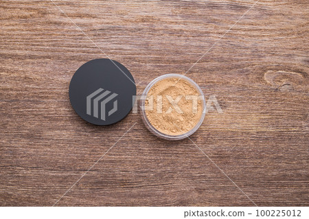 Container of loose mineral face powder for skin tone on wooden background, close-up top view 100225012