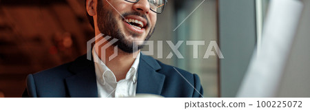 Close up of smiling unrecognisable businessman drinking coffee and working laptop in cafe 100225072