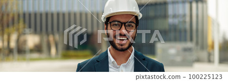 Indian construction architect in suit and hardhat with paper folder in hands against modern building Indian construction architect in suit and hardhat with paper folder in hands against modern building 100225123