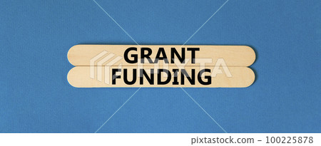 Grant funding symbol. Concept words Grant funding on wooden stick. Beautiful blue table blue background. Business and grant funding concept. Copy space. 100225878