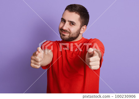 Close up portrait of young attractive man wearing red t shirt pointing at camera isolated purple background, handsome bearded guy looking smiling at camera and pointing with his index fingers. 100230906