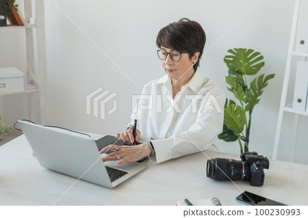 Mature intelligent woman working with computer and graphic tablet and stylus. She is a successful self employed retoucher and photograph 100230993