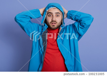Handsome young man with wearing blue coat and red shirt standing and touching his head, looking directly at camera with big eyes, being very shocked. 100231005