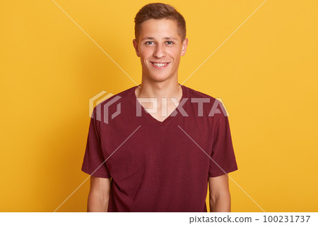 Close up portrait of smiling handsome man with blond hair, wearing in burgunde casual t shirt, standing and looking at camera, isolated on yellow studio background. Copy space for avertismant. Close up portrait of smiling handsome man with blond hair, wearing in burgunde casual t shirt, standing and looking at camera, isolated on yellow studio background. Copy space for avertismant. 100231737