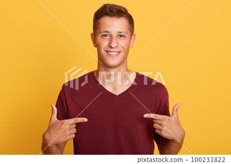 Close up of handsome man in blank burgundy t hirt pointing at himself isolated over yellow studio background, male with pleasant appearance looking smiling ditectly at camera. Advertising concept. Close up of handsome man in blank burgundy t hirt pointing at himself isolated over yellow studio background, male with pleasant appearance looking smiling ditectly at camera. Advertising concept. 100231822