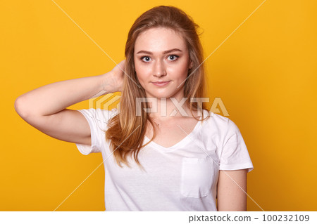 Closeup portrait of positive energetic young lady touching her hair with one hand, looking directly at camera, having pleasant facial expression, standing isolated over yellow background, being calm. Closeup portrait of positive energetic young lady touching her hair with one hand, looking directly at camera, having pleasant facial expression, standing isolated over yellow background, being calm. 100232109