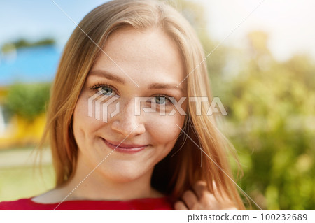 Close-up portrait of fair-haired woman with green alluring eyes, freckles smiling having dimples on cheeks looking happily directly into camera isolated over green background standing outdoors 100232689