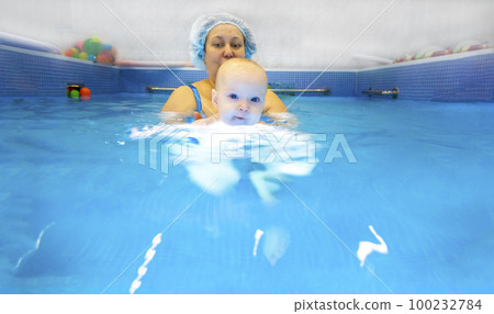 Adorable baby girl enjoying swimming in a pool with her mother early development class for infants teaching children to swim and dive.  100232784
