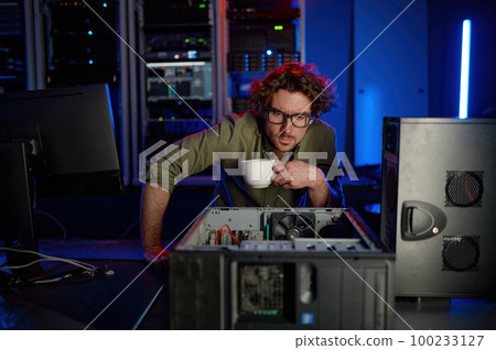 Repairman with cup of coffee looking at disassembled computer system unit 100233127