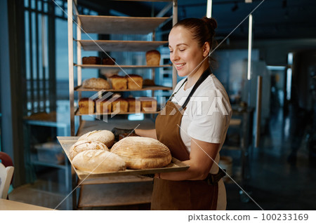 Pretty woman baker holding variety of baked bread on tray Pretty woman baker holding variety of baked bread on tray 100233169