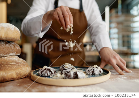 Baker chef sprinkling freshly baked oatmeal cookies with cereals 100233174
