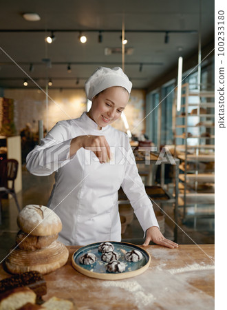 Baker chef sprinkling freshly baked oatmeal cookies with cereals 100233180