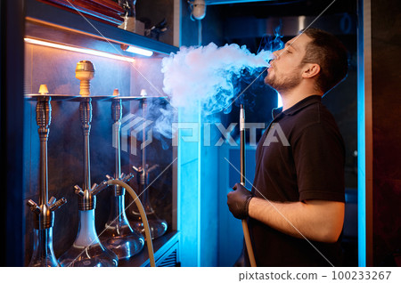 Young man smoking at hookah bar while preparing equipment for client Young man smoking at hookah bar while preparing equipment for client 100233267