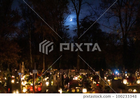 At night in the cemetery celebrating All Hallows' Day with gravestones and candles under the Moon. 100233348